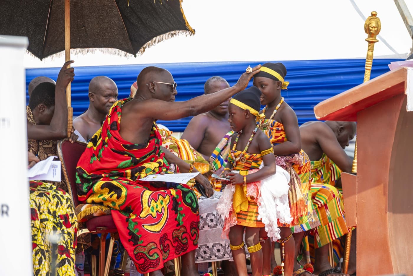 A elder blesses young dancers in kente at the ceremony