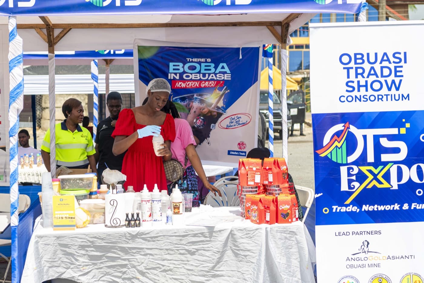 A vendor prepares drinks at the Boba in Obuase stand beside the OTS Expo banner
